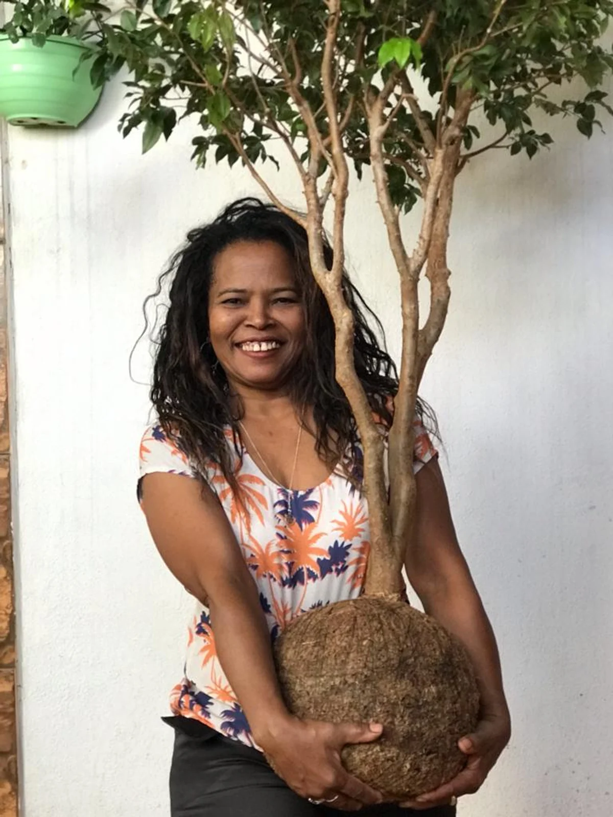 Christianne Marie sorrindo ao lado de uma kokedama de grande porte